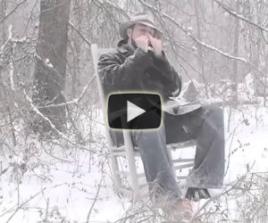 Seduto sulla neve suona un brano con la propria armonica