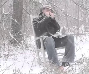 Seduto sulla neve suona un brano con la propria armonica